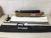 The full contents of the lot showing the Neewer light stand box, white reflector panel, metal rods, mounting bracket parts, and the Neewer branded carrying bag.