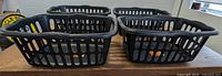 Four black Sterilite rectangular laundry baskets arranged in two rows of two on a floor, showing size and ventilation slots on sides.
