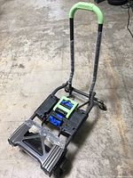 Shifter Multi-position folding hand truck and cart standing upright with handle wrapped in plastic and loading platform extended on a concrete floor.