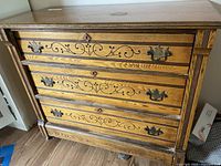 Front close-up of wooden dresser showing decorative inlay on drawers and vintage brass handles.