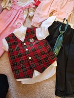 Close-up photo of baby boy formal outfit including white shirt, plaid vest with buttons, black pants, and green necktie