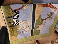 Quilted baby crib comforter showing zebra, elephant, giraffe, and palm trees in pastel colors.