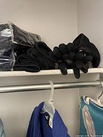 Shelf with folded black North Face fleece jacket, black fleece blankets wrapped in plastic, and several pairs of black gloves.