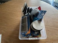 Photo showing a plastic container filled with assorted black, gray, and beige round felt pads and sliders for furniture legs of various sizes.
