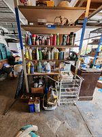 Wide shot of garage shelving unit with assorted garage and garden maintenance products, rope ladder, hedge trimmer, and containers stacked and stored.