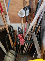 Photo showing yard tools including sledge hammer, shovels, pick axe, shop light, extension cord, and miscellaneous tools organized in a tool holder against pegboard