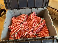 Multiple folded pairs of red and white striped fleece pajamas with green trim in a plastic bin.
