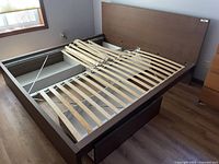 Full view of IKEA king size bed frame with mattress support wooden slats and built-in storage drawers beneath the frame. One drawer is open and damaged.