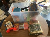 Plastic tub filled with assorted children's toys including a toy rotary phone, flash cards, puzzle book, and part of a baseball bat visible inside the tub.