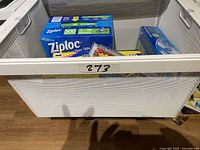 Photo showing the lot's assorted boxes of kitchen storage items including Ziploc bags in a white mesh basket.