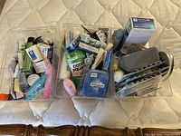 Photo of three plastic bins filled with various assorted bathroom items such as toothpaste, teeth whitening strips, deodorant sticks, and cotton swabs.
