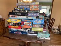 Photo showing a large assortment of board games stacked on a wooden table, comprising classic family and kids games.