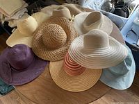Photo of 8 assorted women's wide brim sun hats in various colors and weave styles displayed on a table.