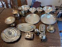 Photo showing entire 15-piece silverplate lot arranged on table including trays, bowls, teapot, covered dishes, and salt and pepper shakers