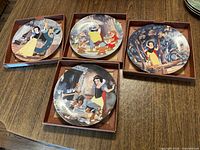 Four Disney Snow White collector plates displayed in open cardboard drawers on wooden surface.