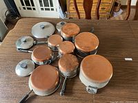 All cookware pieces together showing copper bottoms and black handles on wooden table.