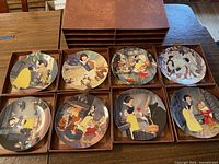 Lot of eight 8.5-inch vintage Walt Disney Snow White Knowles collector's plates displayed in a brown 8-drawer cardboard storage case on a wooden table