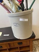 Marshall Pottery 5-gallon stoneware crock used as umbrella stand with umbrella handles visible inside, showing chip on rim and number label 341