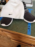 Adidas sneakers in black with white soles and elastic striped band with white Nike beanie on top, showing size label 8.5, photo taken on kitchen counter.