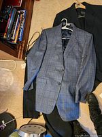 Light blue plaid Jos A. Banks suit jacket on top of dark pants and black coat on floor with part of room visible