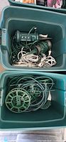 Bin filled with coiled green and white extension cords and green outdoor power stakes with sockets and switches
