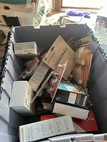 Photo of large gray plastic tub filled with assorted boxed and blister-packaged light bulbs, showing visible labels and packaging types.