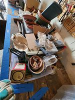 Wide shot showing assortment of potting and gardening items including stacked plastic and terracotta pots, gloves, tools and small containers on a table.