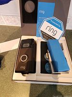 Ring WiFi doorbell camera sitting in its original box alongside instruction manual, security sign, and accessory box.