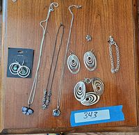 Photo showing various silver 925 stamped jewelry pieces on a wooden surface including necklaces, earrings, bracelets, and a ring, arranged neatly with a lot number tape.