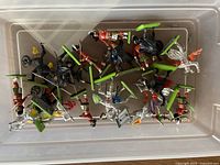 Overview photo of all metal figurines in a plastic container, showing knights and Beefeaters in varied poses and colors on green bases.