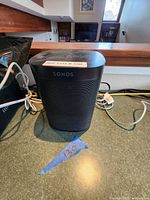 Black Sonos One smart speaker in used condition with power cable visible, showing general wear and dust.