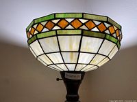 Close up photo of the top bowl-shaped stained glass Tiffany style lampshade. Shows white grid pattern with green and orange diamond accents.