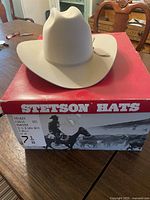 Front view of beige/tan Stetson Rancher cowboy hat sitting on red Stetson hat box with size label 7 1/8 and 3.5 inch brim noted.