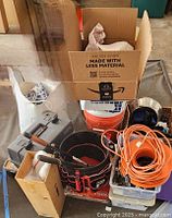 Overall lot showing tool box, black and red tool bucket, orange extension cords, cardboard box, and 5 gallon bucket.