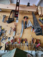 Wide view of pegboard with assorted hand tools including saws, levels, screwdrivers, pliers, hammer, and wrench.
