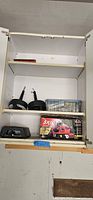 Shelf containing two sewer drain snakes, plastic box of small miscellaneous items, black electronic air pump, and boxed Skil orbital sander.