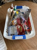 White plastic bin with assorted adhesive items including Loctite Glass Glue, 3M Command strips, tubes of glue, and rolls of tape.