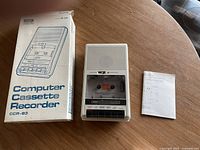 Tandy Computer Cassette Recorder CCR-83 on a wooden round table with original box and a printed instruction sheet visible