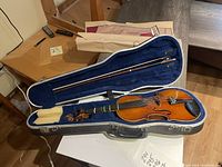 Violin and bow inside an open hardshell case, blue velvet lining visible