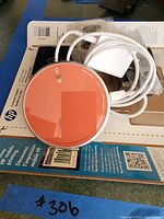 Photo of the wireless charging dock with an orange top surface and white charging cable on top of HP product packaging.