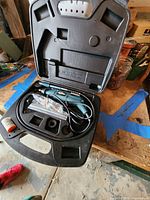 Wizard rotary tool in open black plastic case with attachments laid out inside, placed on a wooden surface near other garage items.