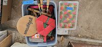 View down into two bins filled with assorted yard games and outdoor game equipment showing paddles, racquets, and colorful game pieces.