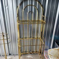 Full view of gold-tone arched metal shelf unit showing frame and three shelves