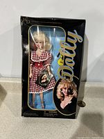 Front view of the boxed Dolly Parton doll in red gingham dress showing packaging with large Dolly logo and image of Dolly Parton.