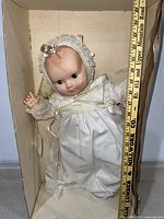 Photo showing the full body of the vintage Effanbee doll in Christening gown inside box, next to a measuring tape indicating 23 inches tall.