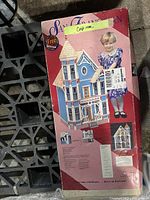 Photo of the front and side of the boxed vintage Dura-Craft San Franciscan Victorian dollhouse kit, showing detailed box art with child's image and full dollhouse illustration.