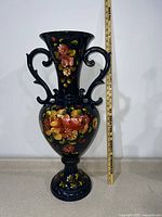 Front view of the vase showing full height with measuring stick Next to it to confirm the 28-inch height and floral design on the body.