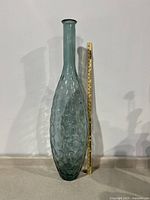 Front view of the tall blue-green dune pattern glass floor vase next to a measuring stick showing its height around 42 inches.