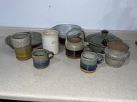 Photo of 10 vintage pottery items including cups, bowls, crocks and pie plate on a countertop