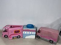 Three Barbie vehicles displayed against a wall: two pink campers on left and right with a white and blue airplane camper in the center.